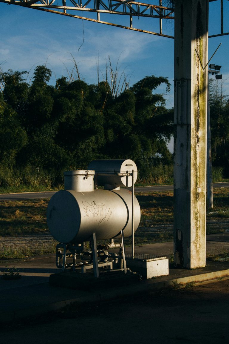 A metal fuel tank outdoors, highlighted by the warm sunset glow, surrounded by trees.